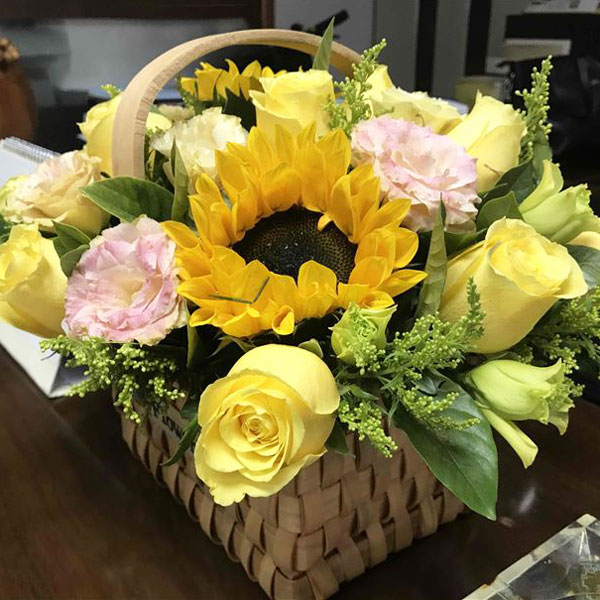 Medium assortment of sunflowers, roses, lisianthus and mixed foliage arranged in a classic hanging basket