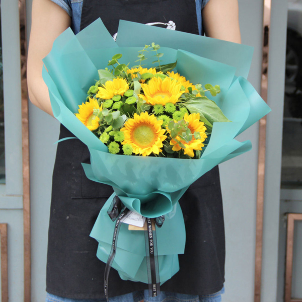 Medium bouquet of 9 sunflowers interspersed with button poms and eucalyptus leaves wrapped in quality matte paper