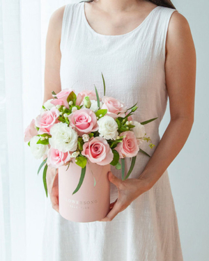 Medium assortment of pink roses, eustomas, jasmine petals, and foliage arranged in a cylinder gift box